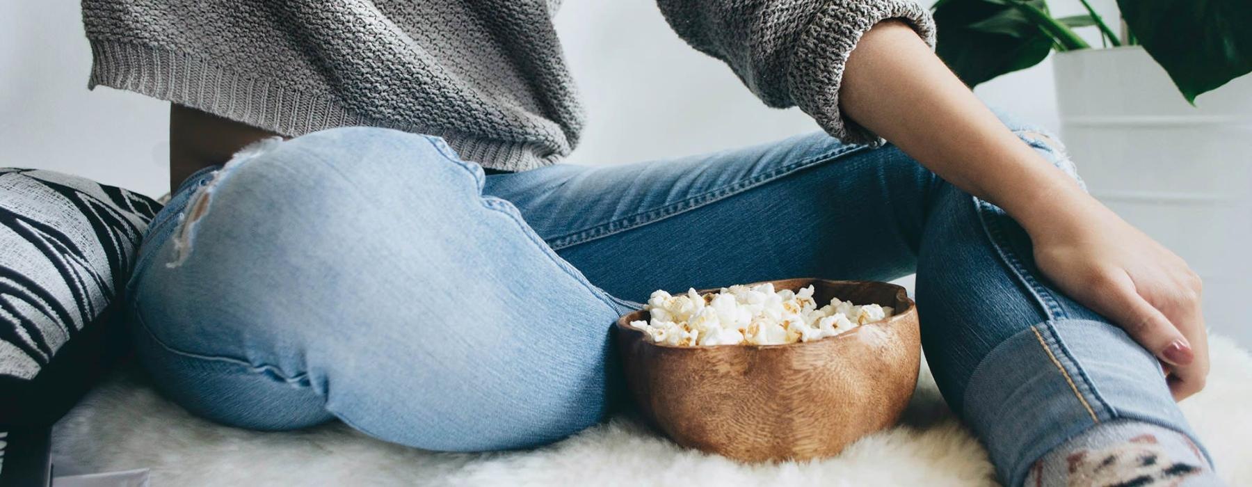 woman sits on a rug with a bowl of popcorn